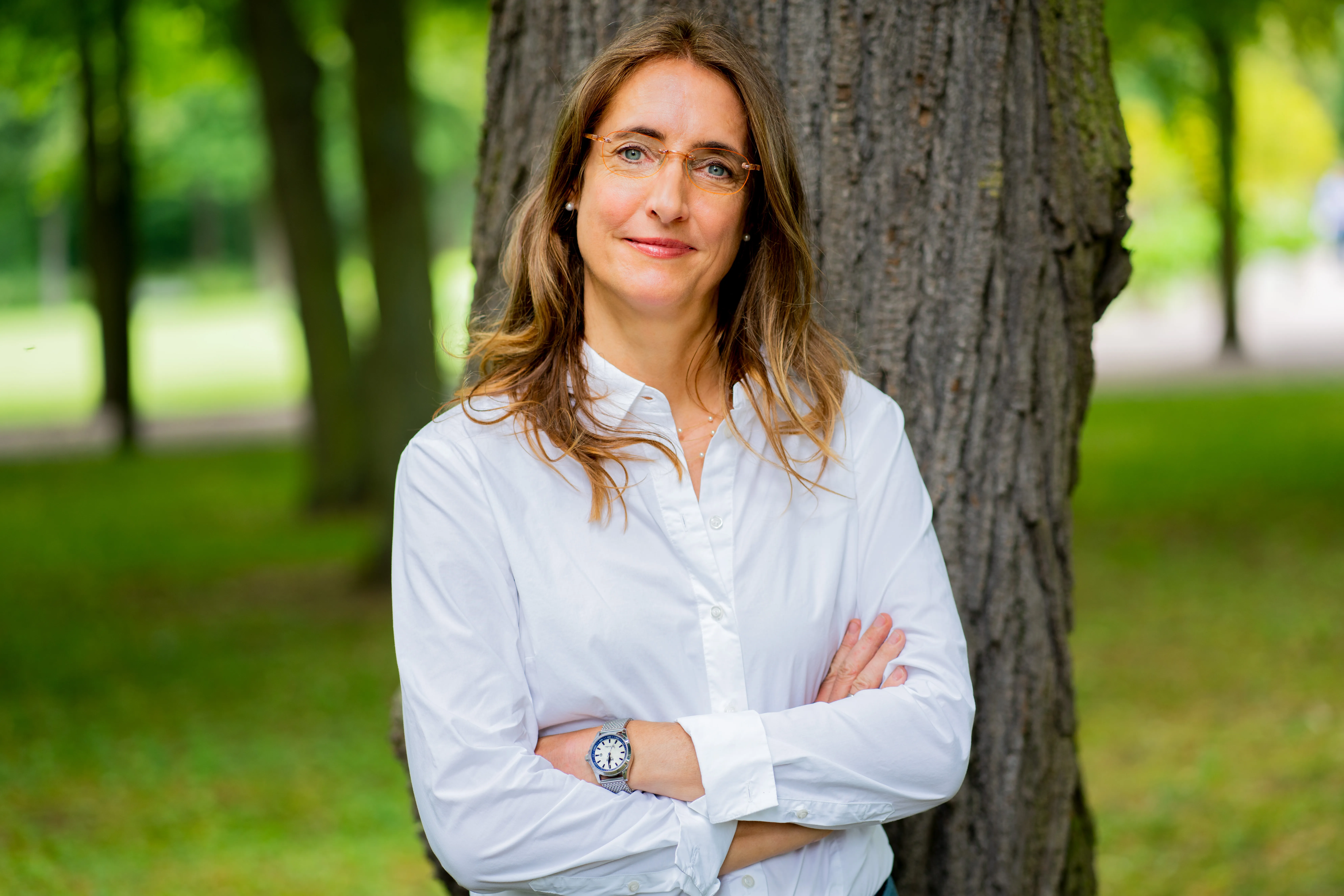 Andrea Sprengart mit verschränkten Armen an einem Baum im Park